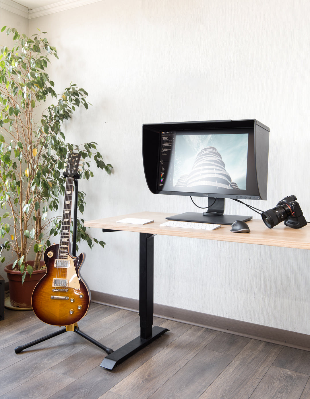 Estación de trabajo de un artista junto a su pantalla de edición, cámara fotográfica, guitarra y escritorio eléctrico